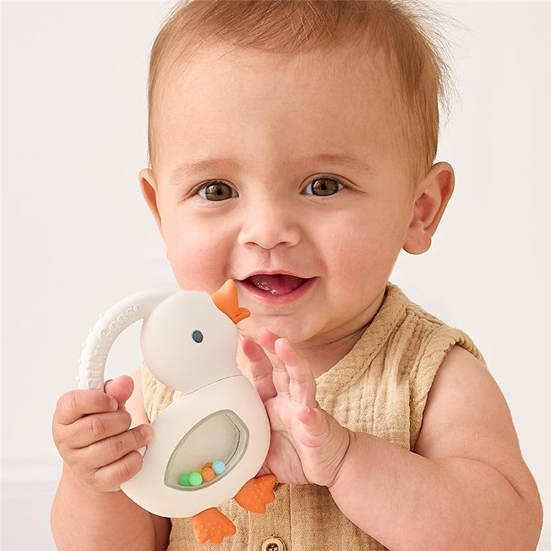 Baby smiling while holding an Itzy Ritzy Shake Silicone Teether featuring Gracie the Goose with colorful beads inside.