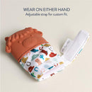 Silicone teething mitten featuring a cow design with colorful patterns, adjustable strap for custom fit, wearable on either hand.