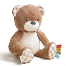 Soft brown bear plush toy designed for newborns, featuring a white tummy, checked ears, and colorful fabric tags.