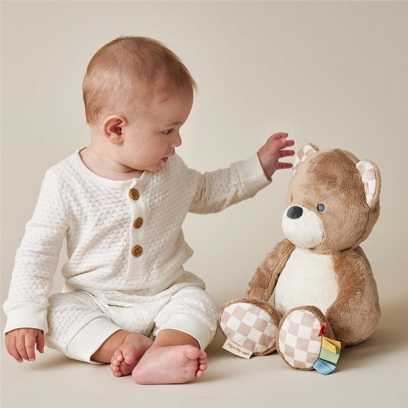 Infant interacting with a soft Itzy Ritzy Snuggles Plush Bear toy, featuring a light brown color and checkered details.