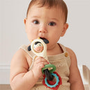 Infant holding an Itzy Ritzy Spinner Rattle shaped like a cow, featuring colorful rings and a smiling face.