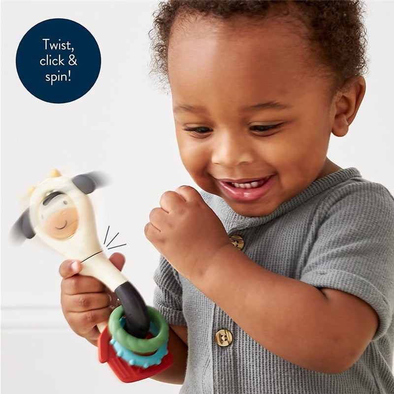 A smiling child holding an Itzy Ritzy Spinner Rattle Cow toy, featuring a spinning cow face and colorful attachments.
