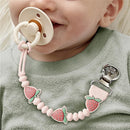 Strawberry-themed silicone pacifier clip attached to a pacifier, held by a smiling baby wearing a green sweater.