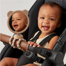 Stroller mirror shaped like a bear reflects a smiling baby in a car seat, gripping the handlebar with colorful teething toys.