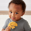 Toddler smiling while holding a yellow Itzy Ritzy Sweetie Shake Plus™ teething and rattle toy shaped like a croissant.