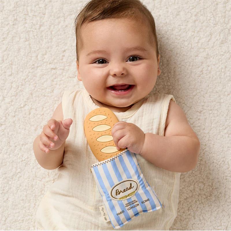 Smiling baby holding the Itzy Ritzy Teensy Crinkle Silicone Sensory Teether shaped like a baguette, against a soft background.