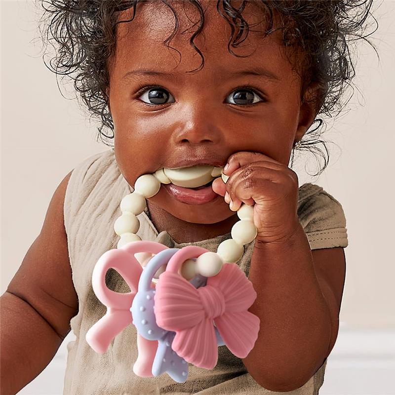 Baby smiling while holding a multi-textured silicone teether featuring colorful bows, safe for chewing and play.