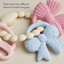 Multi-textured silicone teether featuring a blue bow, pink bow, and textured beads for soothing sore gums.