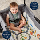 Two-in-one play mat with town scene and taupe checkerboard, featuring a seated baby in a wagon with safety buckles.