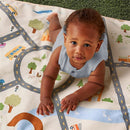 Baby playing on Itzy Ritzy Wagon to Floor 2-in-1 Play Mat featuring a town scene and taupe checkerboard design.