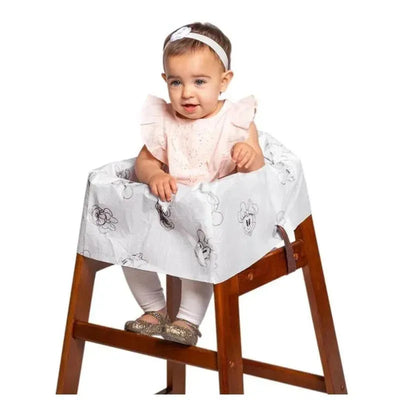 A toddler sits in a wooden high chair covered with a Disney Baby disposable cover featuring character illustrations.
