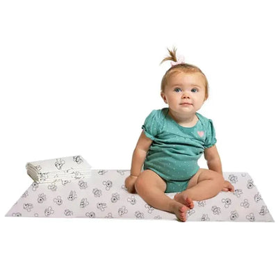 24Pk Disney Baby Disposable Changing Pads displayed with a baby sitting on one pad, wearing a teal outfit with a pink heart.