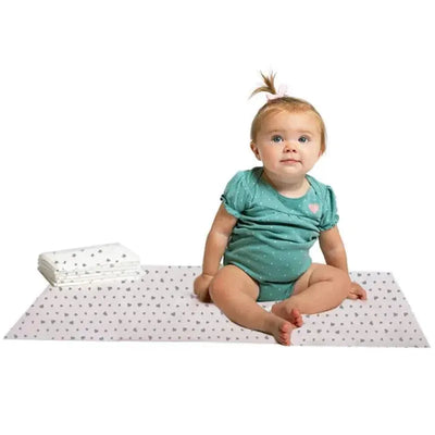 Toddler sitting on a J.L. Childress disposable changing pad with polka dots, next to a stack of additional pads.