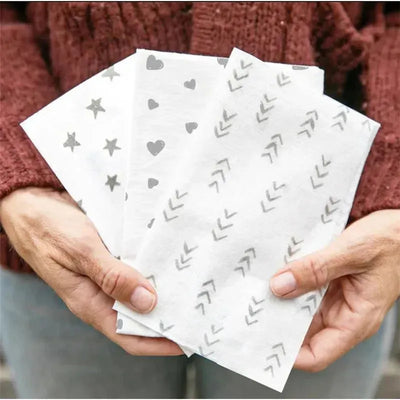 Disposables changing pads in various designs including stars, hearts, and arrows, held by a person in a knitted sweater.