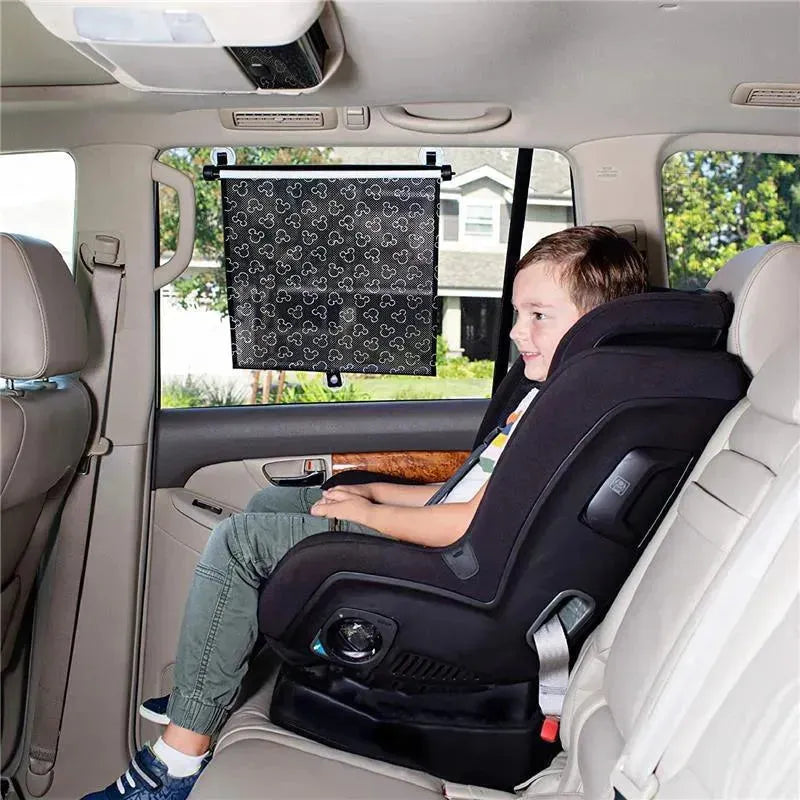 Disney Baby Pull-Down Car Sun Shade featuring Mickey Mouse design installed in a vehicle, while a child sits safely in a car seat.