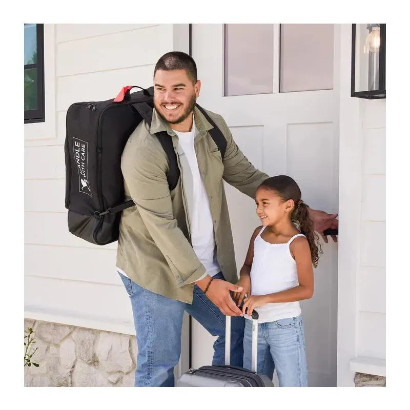 A man with a black travel bag smiles at a young girl holding a rolling suitcase at a front door.