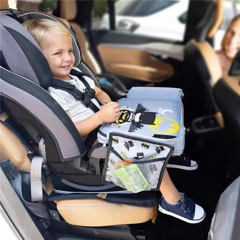 Child in a car seat using a Batman-themed travel tray with a mesh pocket holding snacks and drinks.