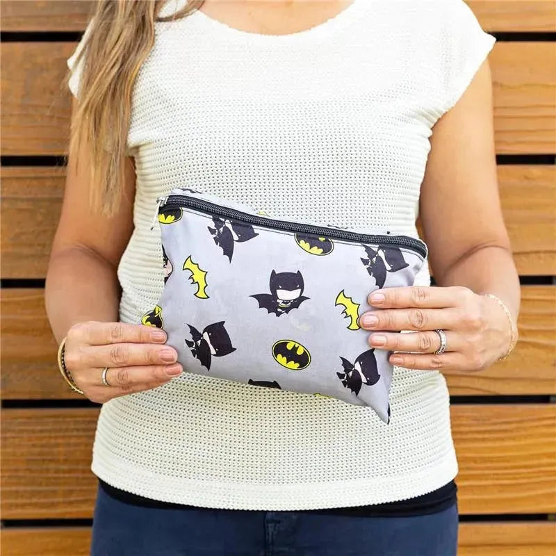 J.L. Childress Batman-themed shopping cart and high chair cover held by a woman, featuring a gray background with Batman graphics.
