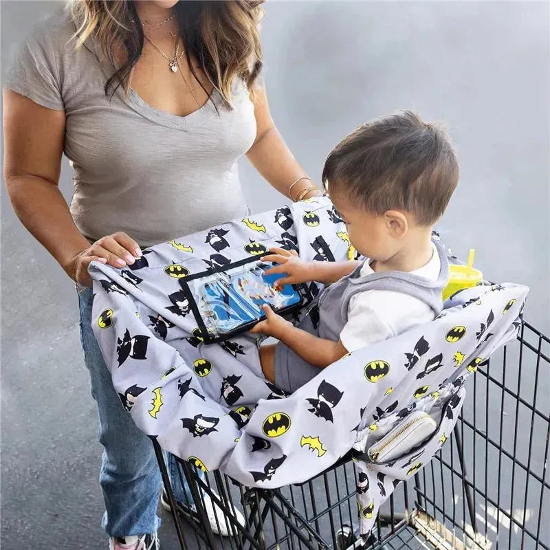Shopping cart cover featuring Batman designs, being used by a toddler watching a tablet while seated inside the cart.