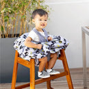 A toddler sits in a wooden high chair, wearing a gray outfit, enjoying a DC Comics Batman shopping cart and high chair cover.