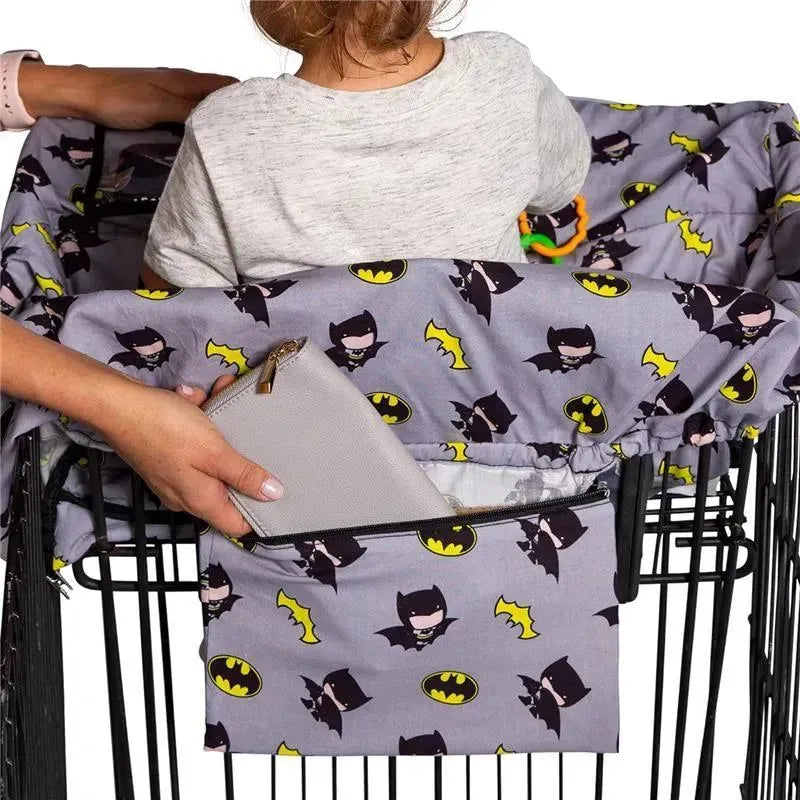 Shopping cart cover featuring Batman designs, with a toddler seated inside and a hand placing a wallet in a side pocket.