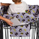 Shopping cart cover featuring Batman designs, with a toddler seated inside and a hand placing a wallet in a side pocket.