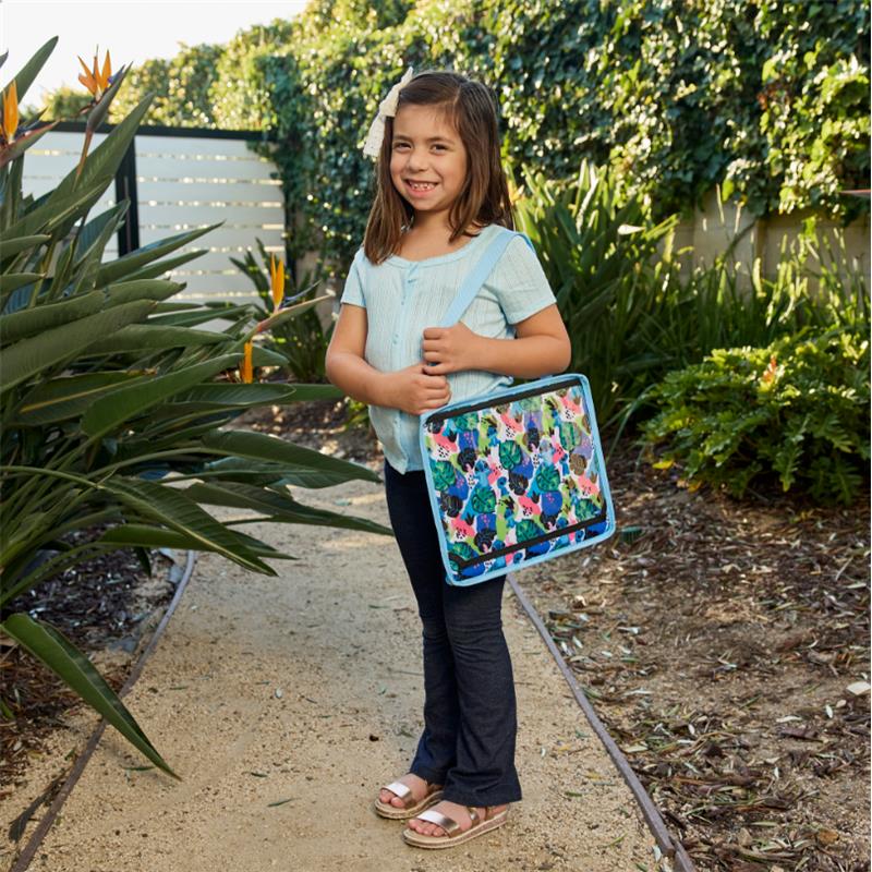 A girl smiling, holding a colorful Disney Baby travel tray with cartoon designs, standing in a garden path.