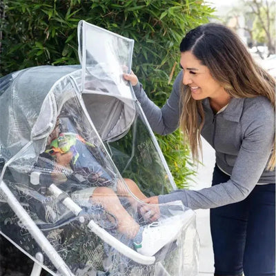 A woman interacts with a child in a stroller covered by the J.L. Childress Healthy Habits Deluxe Weather Shield.