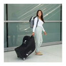 Black J.L. Childress car seat travel bag with wheels, carried by a woman in an airport terminal.