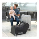 J.L. Childress Premier Infant Car Seat Travel Bag in black, with wheels, next to a man holding a baby at an airport.