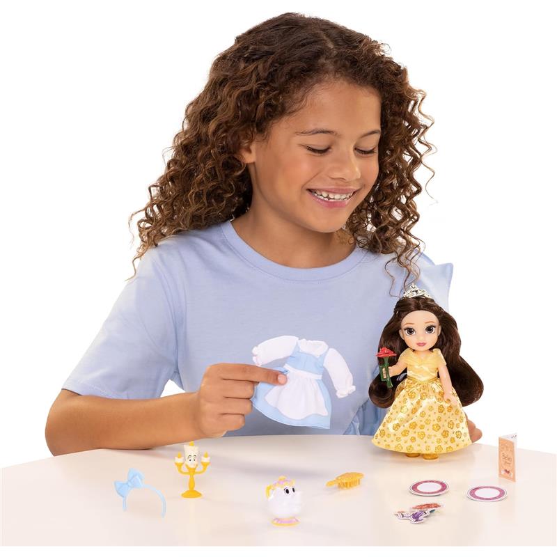 Child holding Belle doll in a yellow gown with accessories, including a blue dress, a teapot, and a candlestick.