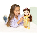 A young girl with long hair is playing with a large Belle doll from Disney, dressed in a yellow gown, while brushing its hair.