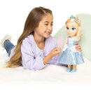 A child smiles while holding a pink wand, playing with a Cinderella large doll wearing a sparkly blue dress.