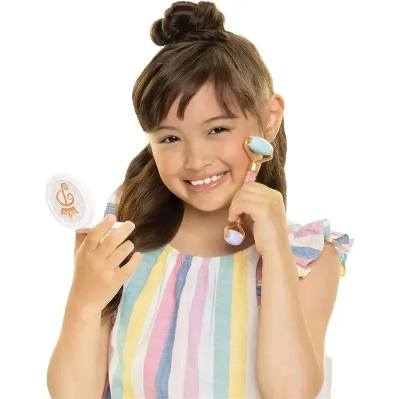 Young girl with long hair holds a mirror and a facial roller, wearing a colorful striped top and smiling.