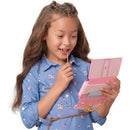 A girl with long hair holds a pink wristlet phone, smiling and holding a lollipop, dressed in a floral blue shirt.