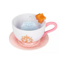 Tea cup and saucer set featuring a pink handle, an orange tea bag, and a blue dress-shaped tea tag.