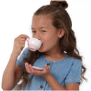 Young girl sipping from a pink-handled teacup, holding a matching saucer, wearing a blue denim shirt.