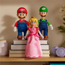 Plush figures of Mario, Luigi, and Princess Peach standing on stacked books, featuring vibrant colors and detailed costumes.