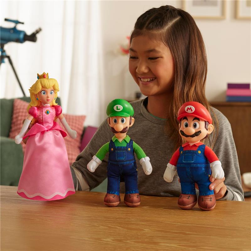 Plush figures of Princess Peach, Luigi, and Mario are displayed on a table with a smiling girl.