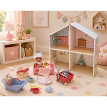 All-vinyl JC Toys doll in crib with accessories including a bath, toys, and a dollhouse backdrop. Bright and playful setting.