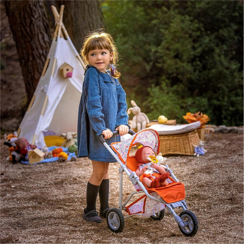Child playing with a bright orange jogger stroller, featuring a doll dressed in cute attire, set against a natural outdoor backdrop.