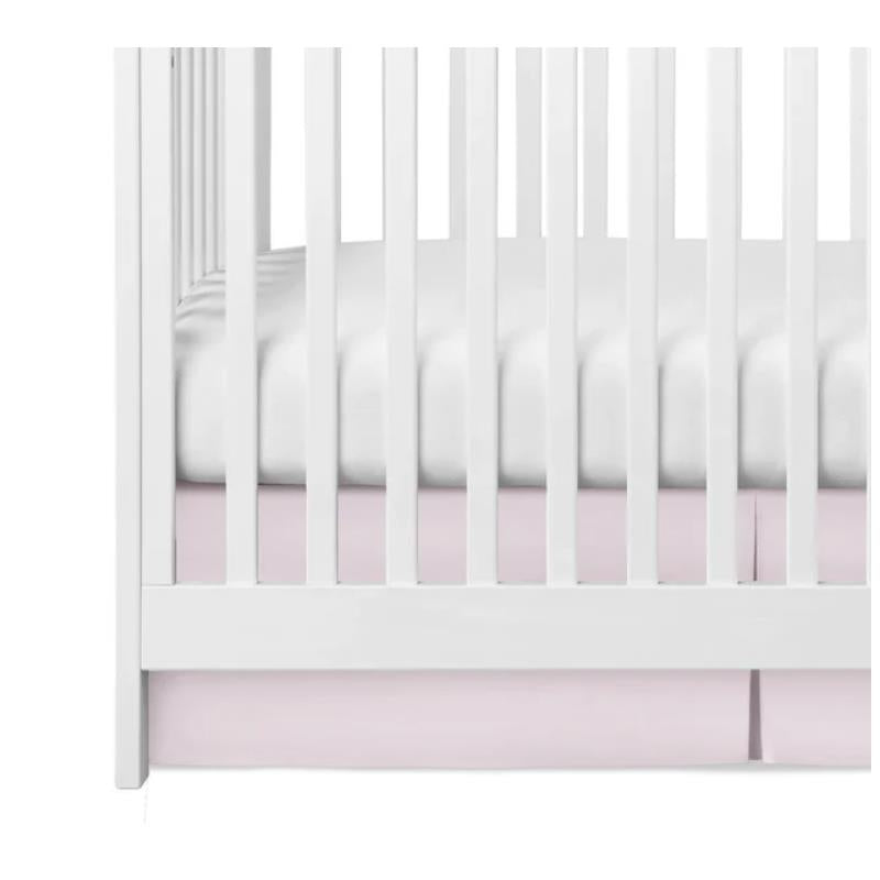 Pleated pink crib skirt positioned under a white crib, enhancing the nursery decor.