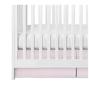 Pleated pink crib skirt positioned under a white crib, enhancing the nursery decor.