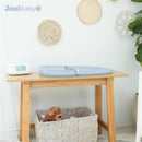 Premium blue changing pad by Jool Baby on a wooden table, alongside a white wipes warmer and a woven basket with a teddy bear.