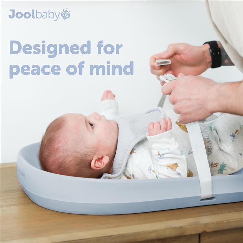 Premium blue changing pad from Jool Baby with a baby wearing a light gray bib, being secured with straps.