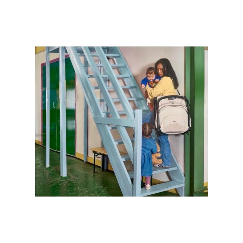 A woman carries a baby and descends stairs while a toddler with a stuffed toy stands below her, showcasing everyday parenting dynamics.