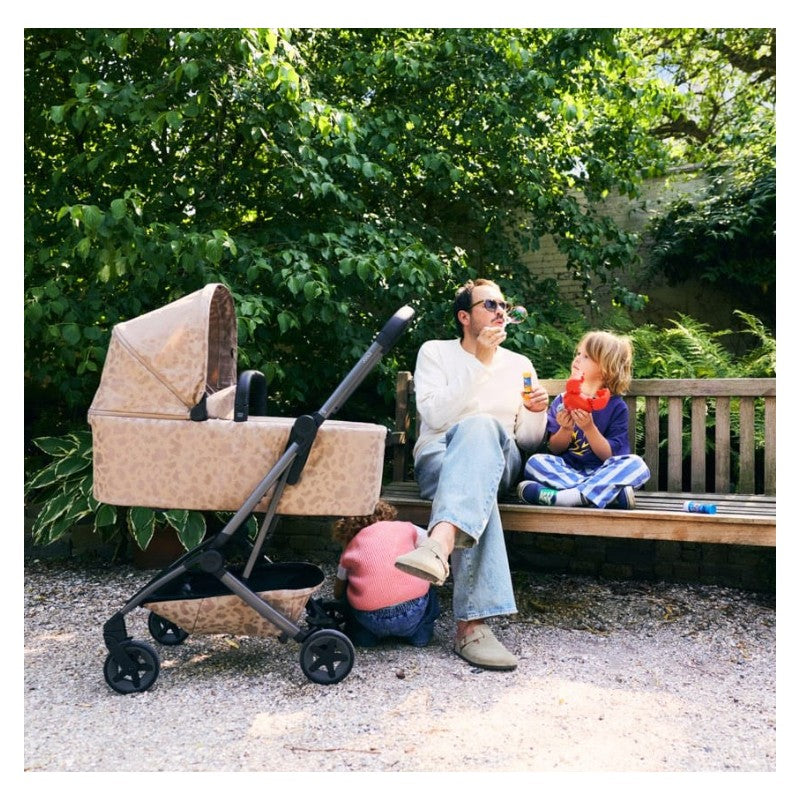 Joolz Aer2 Fold Cot in Chic Renaissance design beside a father and children playing with bubbles on a bench.