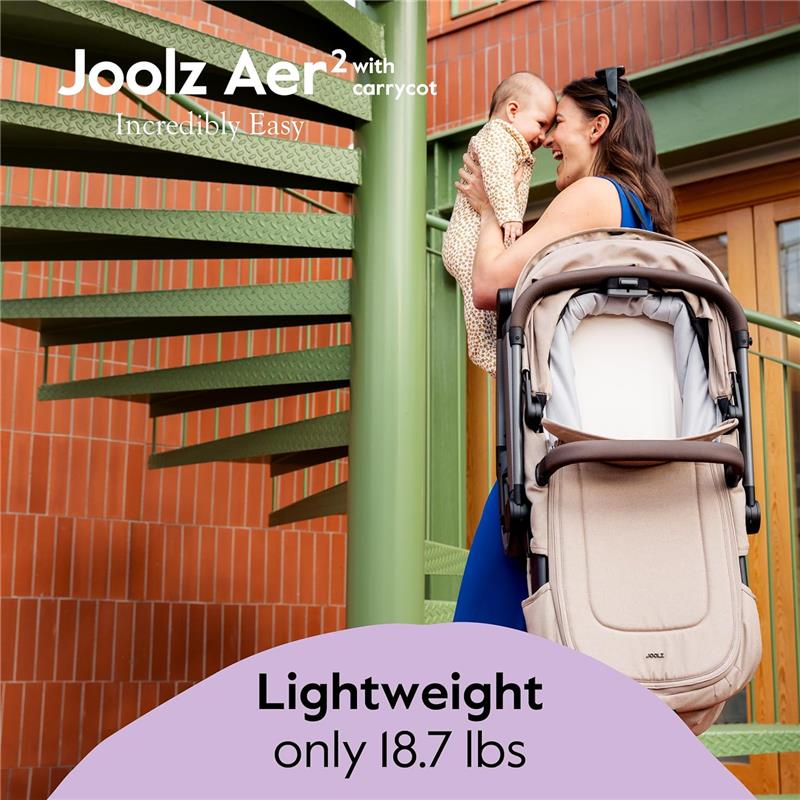 Mother holding a baby near a Joolz Aer2 foldable bassinet, showcasing its lightweight design of 18.7 lbs.