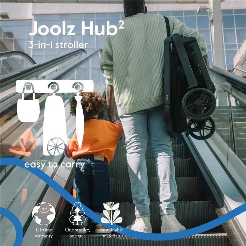 Lightweight Joolz Hub² compact stroller in forest green, carried by a person on an escalator with a child beside them.