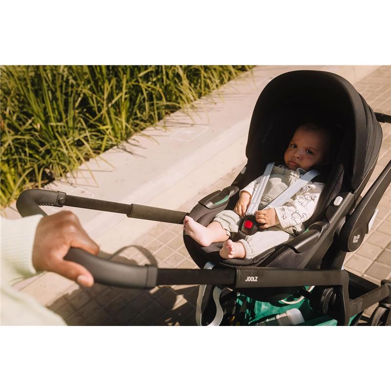 Car seat adapter set for Joolz Hub2 stroller with a baby seated in the car seat, securely fastened, on a sidewalk.